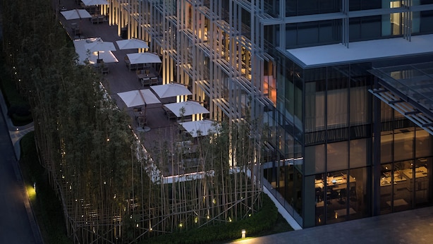 Un hotel moderno con terraza en la azotea, mobiliario exterior y fachada de vidrio.