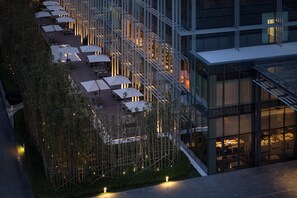 Un hotel moderno con terraza en la azotea, mobiliario exterior y fachada de vidrio.