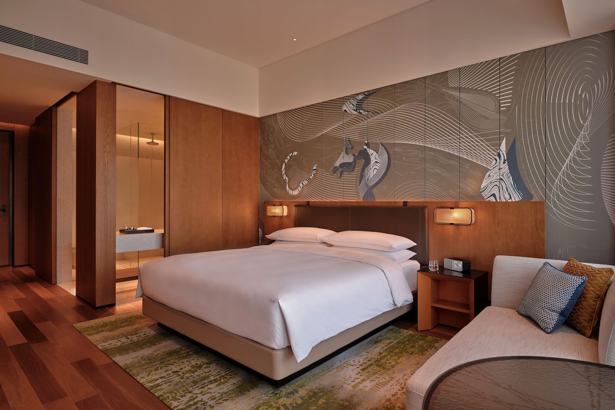 Una habitación de hotel moderna con una cama grande, un sofá, una mesita y un panel decorativo en la pared.