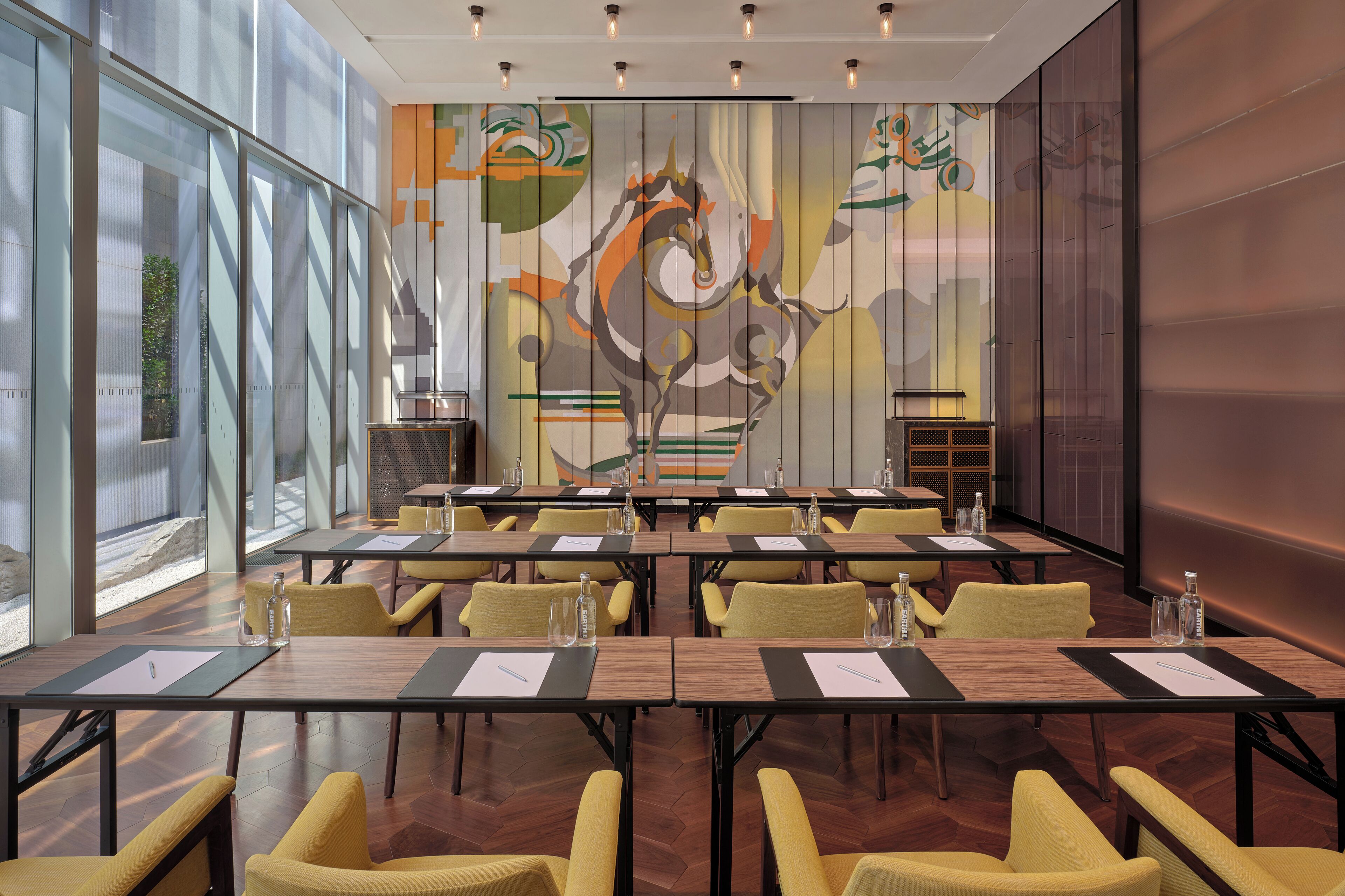 A conference room with multiple tables and chairs, large windows, and a decorative mural on the wall.