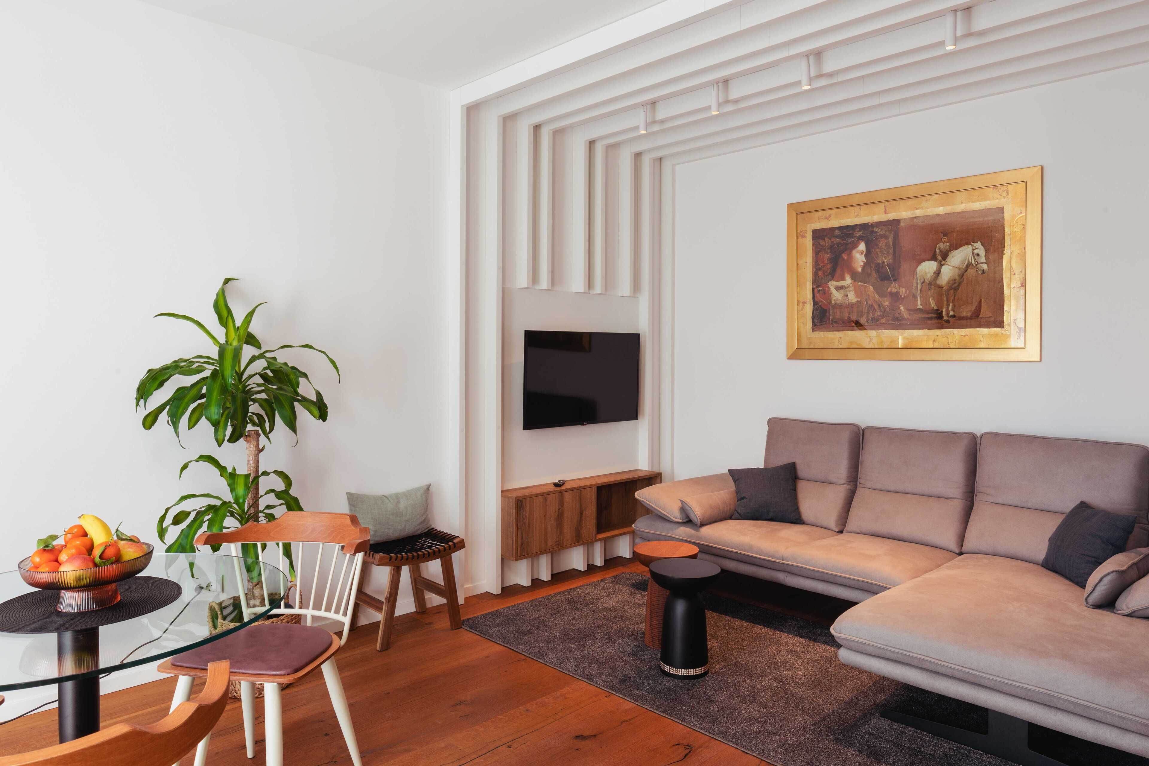 Una sala de estar moderna con un sofá, una mesa de comedor con sillas, un televisor montado en la pared y un cuadro.