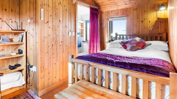 A wooden cabin bedroom with a bed, a shelf with items, and a window. - Seaside Log Cabin, Carna (Carna)