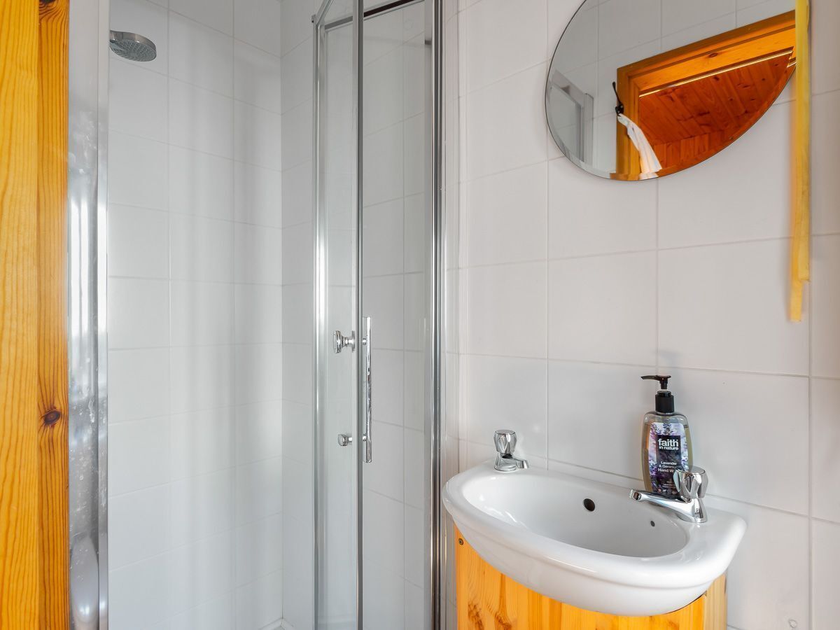 Un baño con cabina de ducha de vidrio, tocador de madera con lavamanos y espejo sobre el lavamanos.