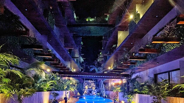 Una piscina interior con una fuente central, rodeada de plantas en macetas y bancos.