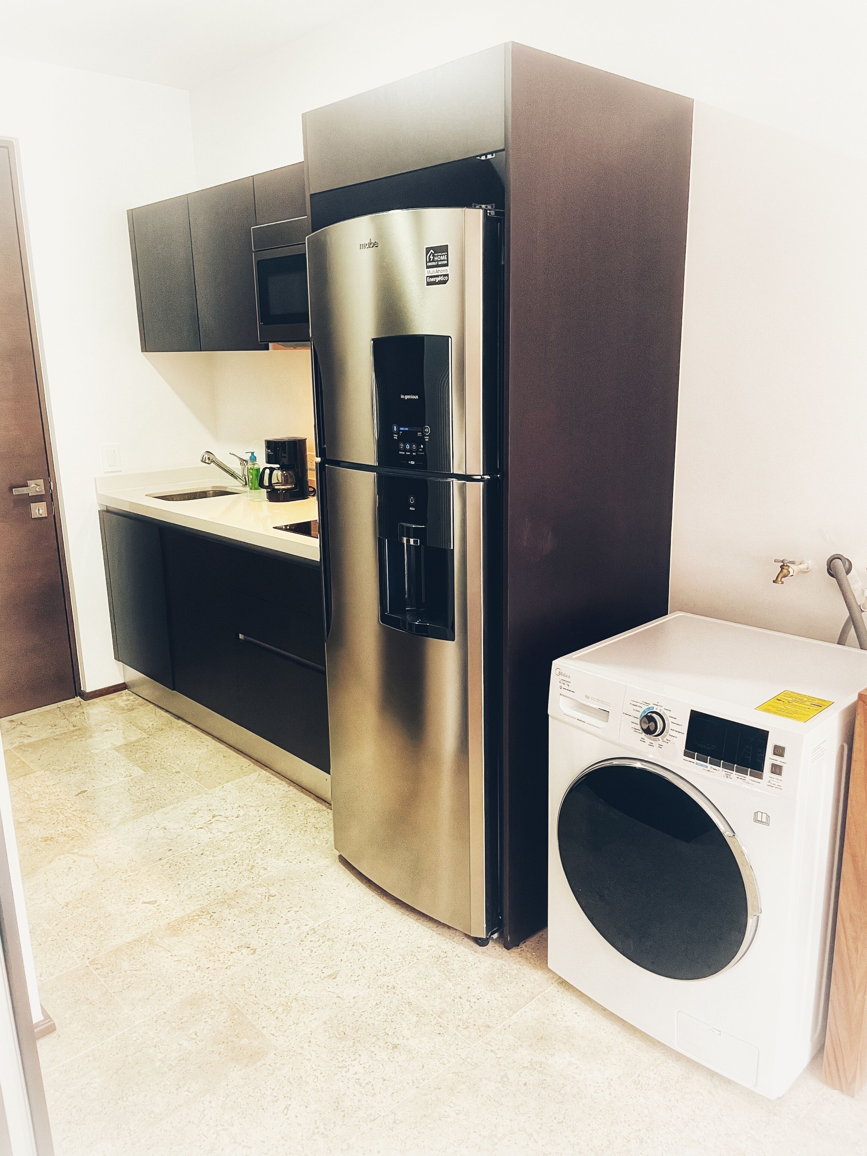 Eine kompakte Küche mit einem Edelstahl-Kühlschrank, einer eingebauten Mikrowelle und einer Frontlader-Waschmaschine.