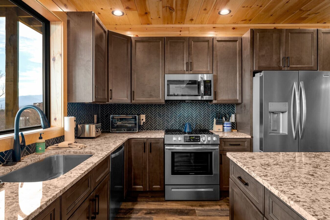 Une cuisine moderne avec des meubles en bois foncé, des appareils électroménagers en acier inoxydable et un dosseret de carrelage disposé en motif chevron.