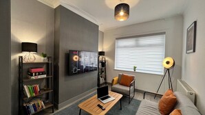 A modern living room with a sofa, coffee table, bookshelf, TV, and a lamp. - Daubney House – Contractors, Families, Holidays (Cleethorpes)