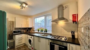 A compact kitchen with a washing machine, microwave, sink, and stove. - Daubney House – Contractors, Families, Holidays (Cleethorpes)