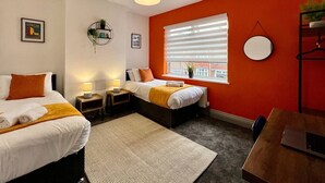 A room with two beds, a window with blinds, a round mirror, and a small table. - Daubney House – Contractors, Families, Holidays (Cleethorpes)