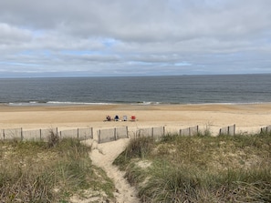 A beach with a wooden fence, a sandy path, and three beach chairs.