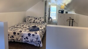 Un dormitorio con una cama, una mesita de noche y una lámpara. Se ve una ventana con vistas al exterior.