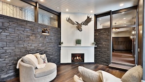 Una sala de estar moderna con una pared de piedra, una chimenea, una cabeza de venado montada y una zona de estar acogedora.
