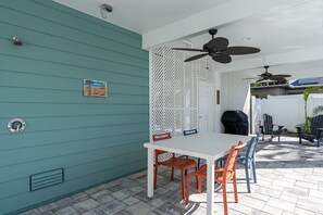 Eine Terrasse mit einem weißen Tisch, orangefarbenen Stühlen, einem Deckenventilator und einem Grillbereich.