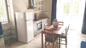Et kompakt køkken med et køleskab, komfur og vask. Der er et spisebord med stole og en stor vase.