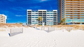 A beachfront hotel with multiple balconies, a sandy beach in the foreground, and a clear blue sky. - Breakers 43 2 Bedroom Condo (Orange Beach)