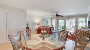 A dining area with a glass table surrounded by chairs, a sofa, and a ceiling fan.