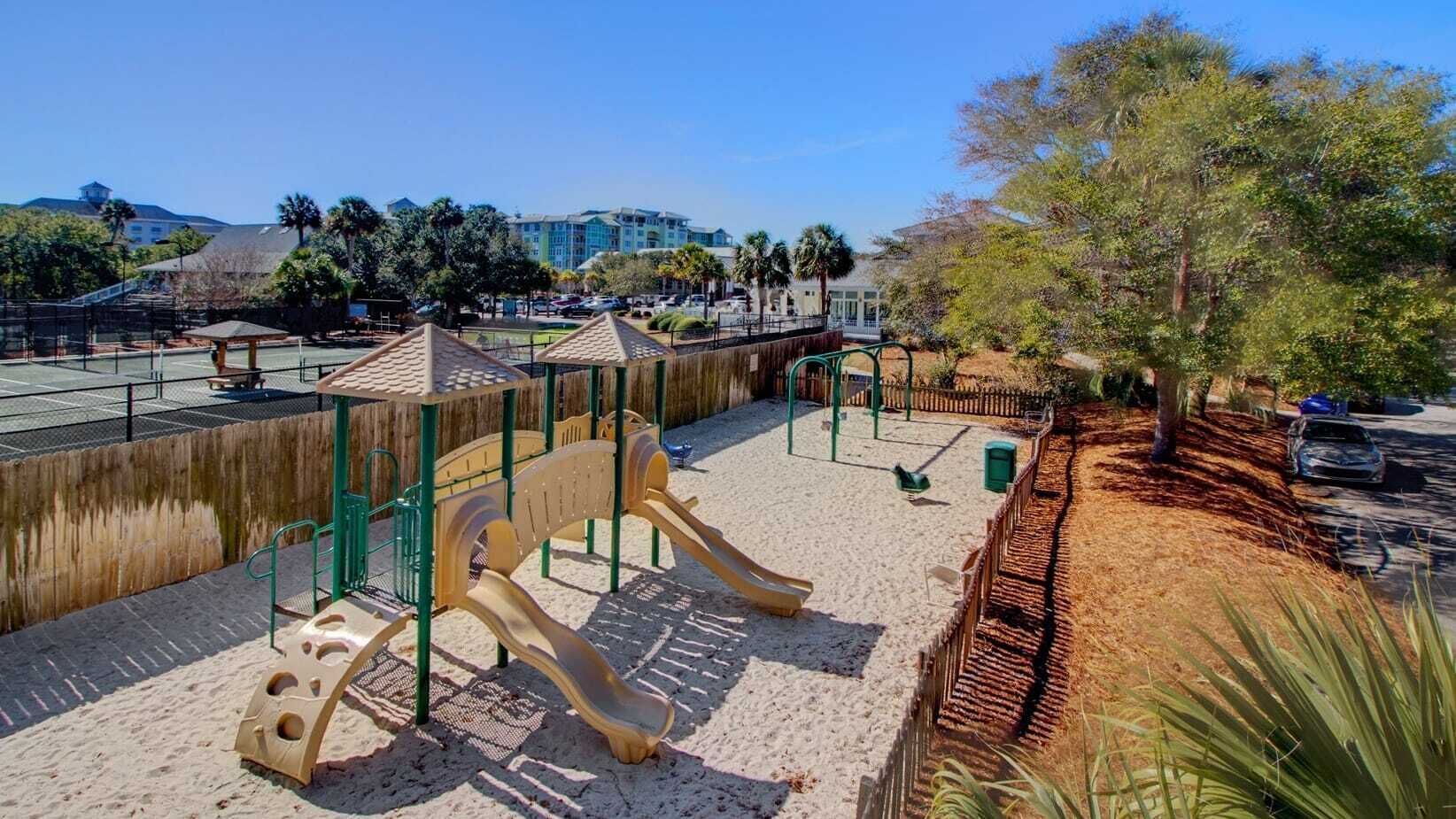 Un parque infantil con toboganes y estructuras para escalar, rodeado de arena y una valla de madera.