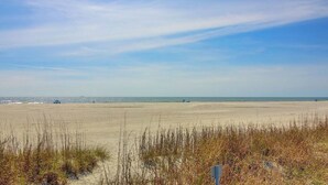 A beach with sand, grass, and a clear sky.