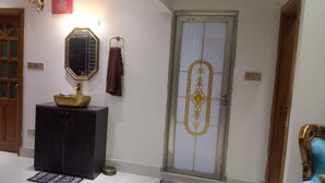 A hallway with a wooden door, a dark cabinet with a gold sink, a mirror, and a decorative door with a gold design. - Stunning 1-bed Apartment in Dhaka Close to Airport (Dhaka)