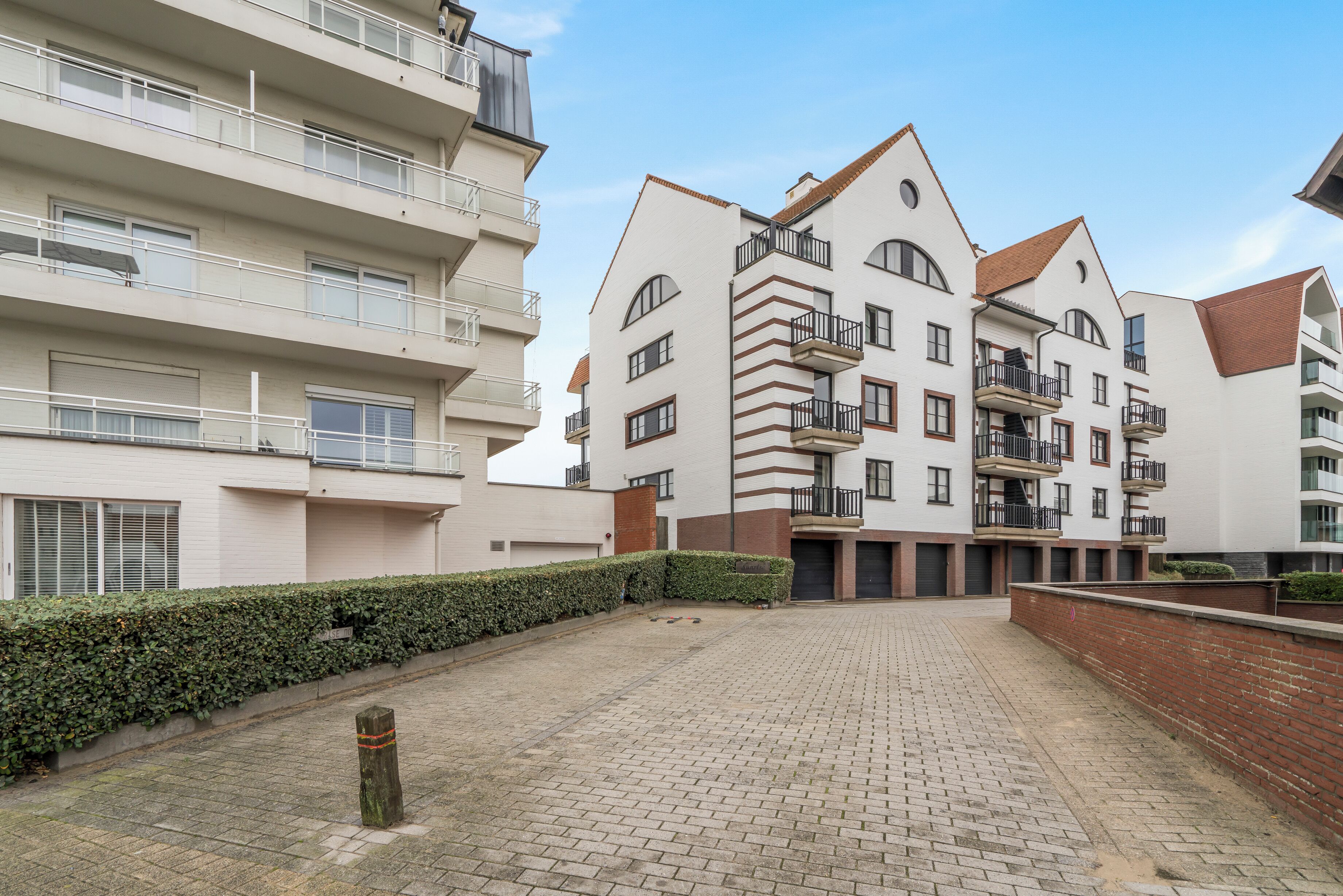 Un edificio residencial de varios pisos con balcones, un patio empedrado y un seto a lo largo del sendero.