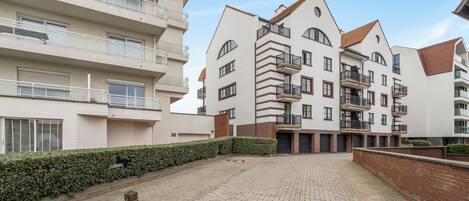 Un edificio residencial de varios pisos con balcones, un patio empedrado y un seto a lo largo del sendero.