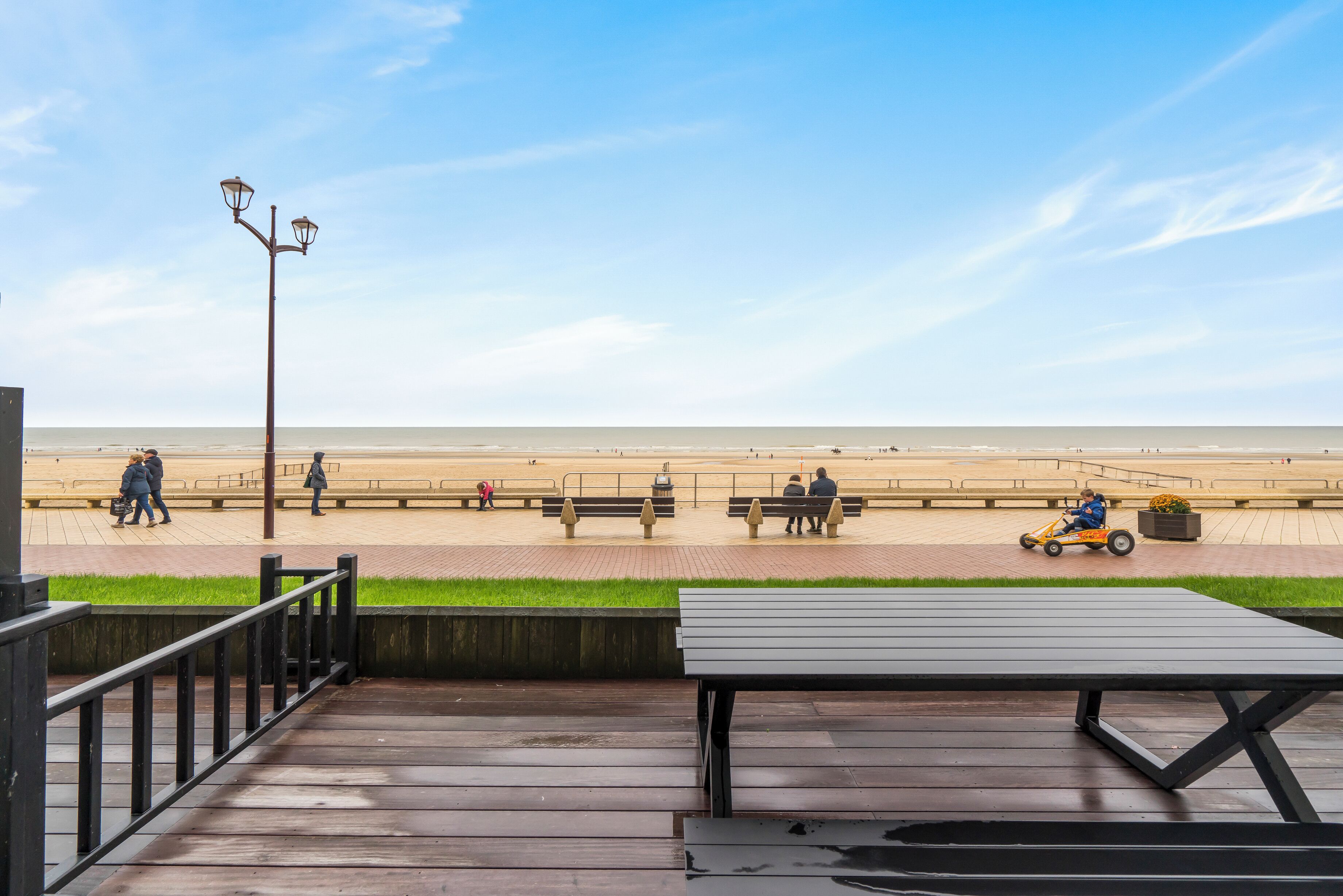 A wooden deck with a bench and a lamppost overlooking a beach.