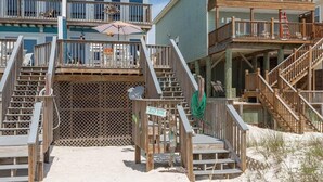 Ein Strandhaus mit Holzbalkonen, die über einen Treppenaufgang erreichbar sind, mit einem Schild, auf dem "Beach House" steht, und einem Sandstrand.