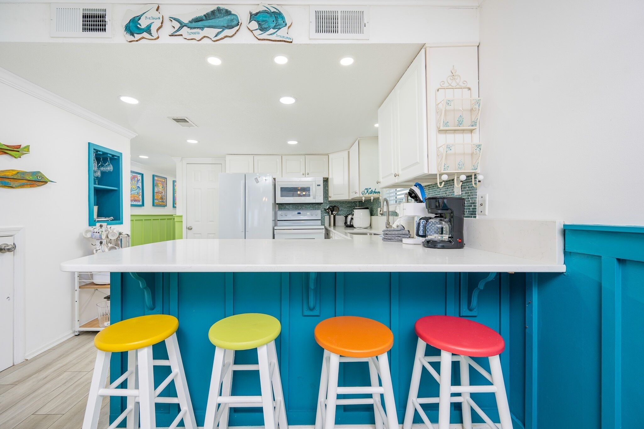 A kitchen with a central island, white cabinets, and colorful stools.