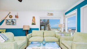 Ein Wohnzimmer mit türkisfarbenen Wänden, einem türkisfarbenen Sofa und einem Couchtisch mit einem Gemälde mit dem Titel "Pelican House Oasis".
