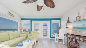 Ein Wohnzimmer mit Blick auf den Strand, einem Deckenventilator, einem Fernseher und einem hellen Sofa.