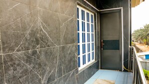 Fachada moderna de mármol oscuro, ventana con marco azul y puerta cerrada.