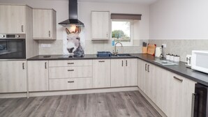 Een moderne keuken met lichte houten kastjes, een roestvrijstalen afzuigkap, een raam met uitzicht en een magnetron.