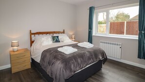 Een slaapkamer met een houten bed, nachtkastjes, een radiator en een raam met gordijnen.