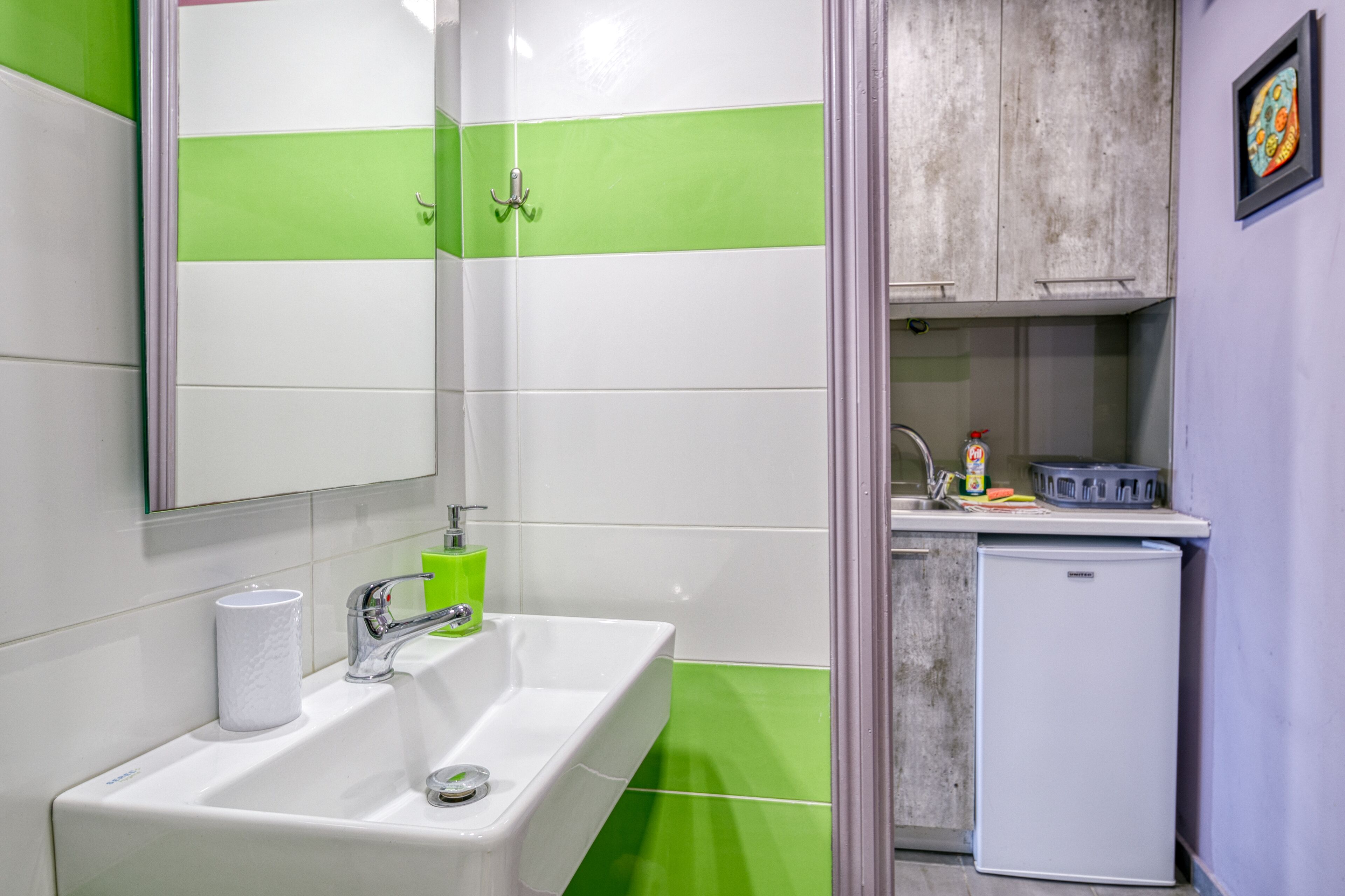 A bathroom with a white sink, green-striped walls, a mirror, a toilet, and a small refrigerator.