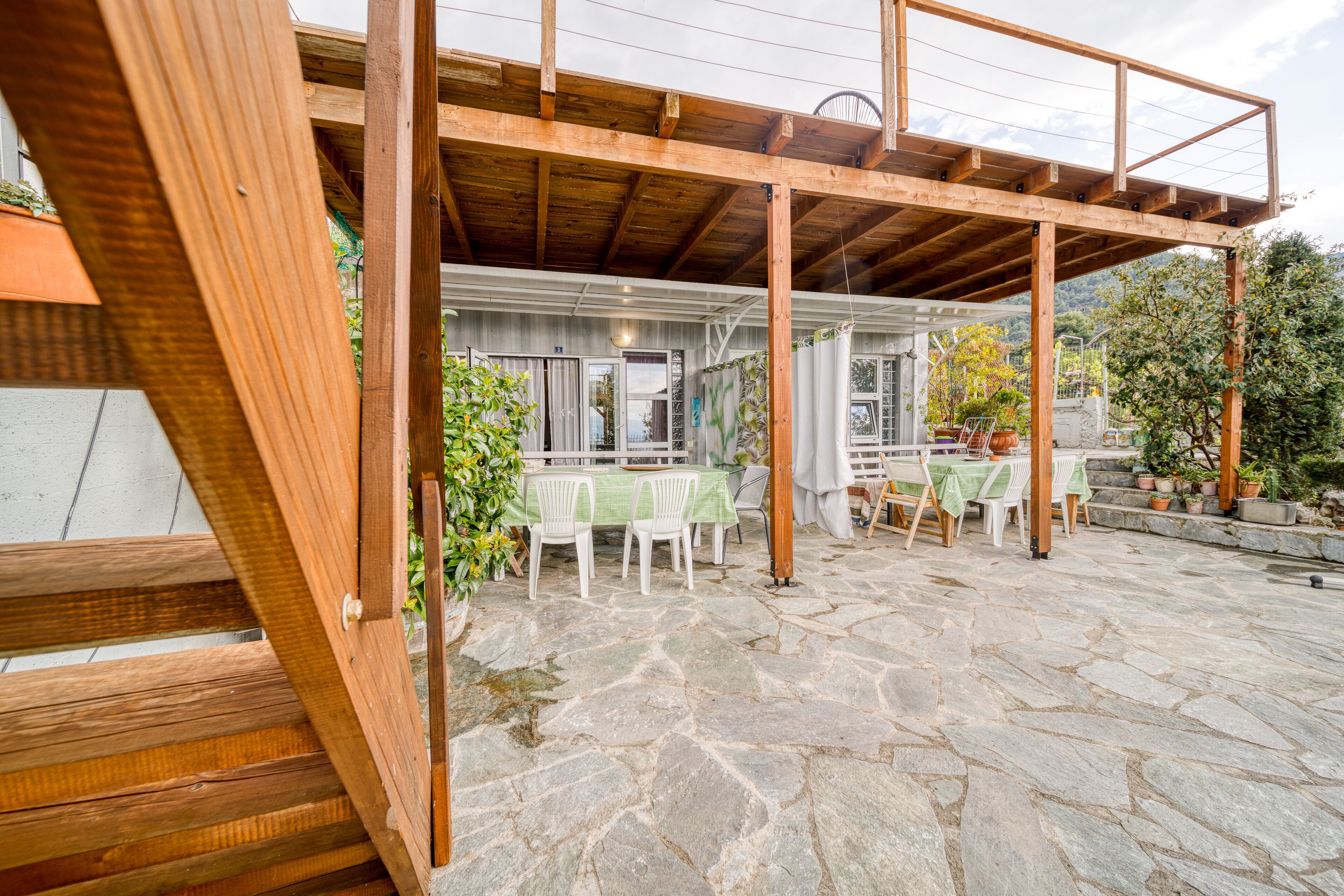 A covered patio area with stone flooring, wooden beams, and a table with chairs.