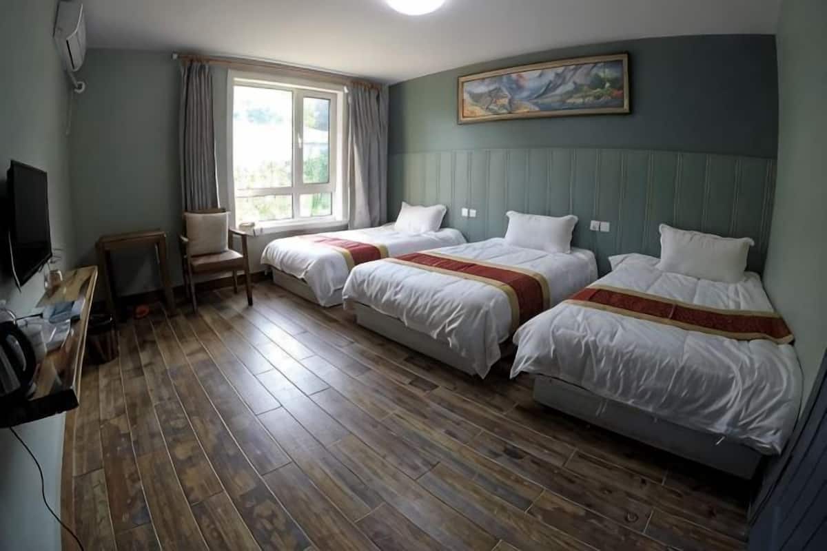 Une chambre avec trois lits, un bureau avec une chaise, une tĂ©lĂ©vision et une fenĂȘtre avec des rideaux.