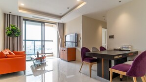 A modern hotel room with a dining area, a sofa, a TV, and a large window offering a city view. - The Rixx Madison (Ho Chi Minh City)