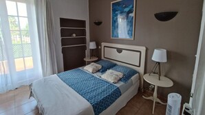 A bedroom with a bed, bedside tables, a painting, and a window with curtains. - Apartment in villa with private pool and garden, 3 bedrooms, warm welcome.  (ANTIBES)
