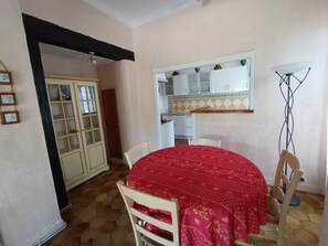 Ein Essbereich mit einem runden Tisch, bedeckt mit einer roten Tischdecke, weißen Stühlen und einer Küche im Hintergrund.