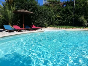 Ein klares Schwimmbecken mit blauem Wasser, umgeben von weißen Kieselsteinen und roten sowie blauen Liegestühlen.