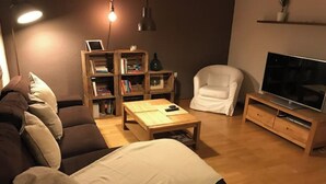 A living room with a sofa, a coffee table, a bookshelf, a white armchair, and a TV on a wooden stand. - MODERN APARTMENT IN THE CENTER (Vilanova i la Geltrú)