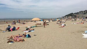 Ein voller Strand mit Menschen, die sich sonnen und spazieren gehen.
