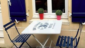 Ein kleiner Tisch im Freien mit einem Schild, zwei Stühlen und zwei Blumentöpfen auf einem Backsteinboden.