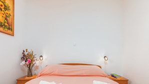 A neatly made bed with pink bedding, two towels on the bed, a vase with flowers on the nightstand, and a painting on the wall. - Apartment Dana (Fazana)