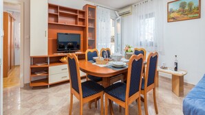 A dining area with a wooden table and chairs, a television, and a painting on the wall. - Apartment Dana (Fazana)