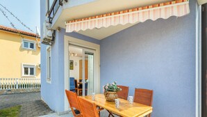 An outdoor patio with a wooden table and chairs, a potted plant, and a striped awning. - Apartment Dana (Fazana)