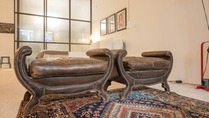 A room with two leather armchairs, a patterned rug, and a large window with blinds. - TOUCHY PORTO - Charming apartment located at Praça da Republica (Porto)