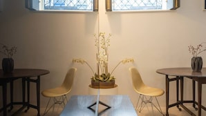 A room with two round tables, each with a single chair. A central plant is placed on a wooden stand between the tables. - TOUCHY PORTO - Charming apartment located at Praça da Republica (Porto)