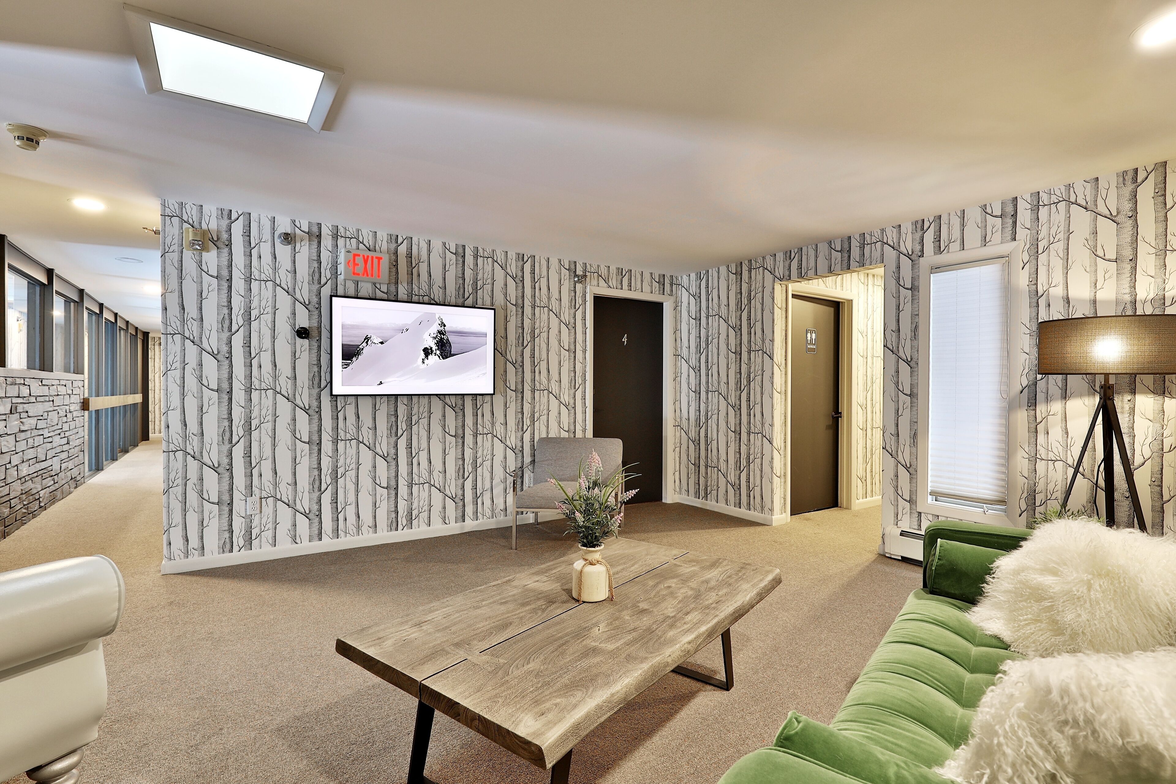 Un salon moderne avec une table basse en bois, un canapé vert et un téléviseur fixé au mur.
