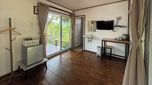 A room with a wooden floor, a white sink, a television, a small table with a chair, and a view through a glass door. - Baan Apa Erawan Resort (Kanchanaburi)